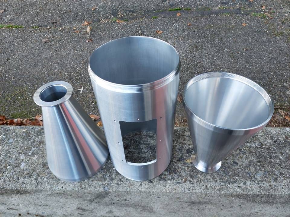 Drei glänzende Metalltrichter und ein Zylinder auf Beton.