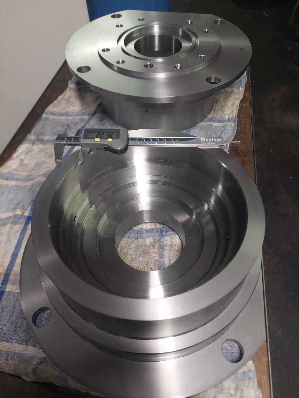 Bearbeitete Metallteile mit einem Messschieber, möglicherweise industrielle Bauteile, auf einer Werkstattfläche.