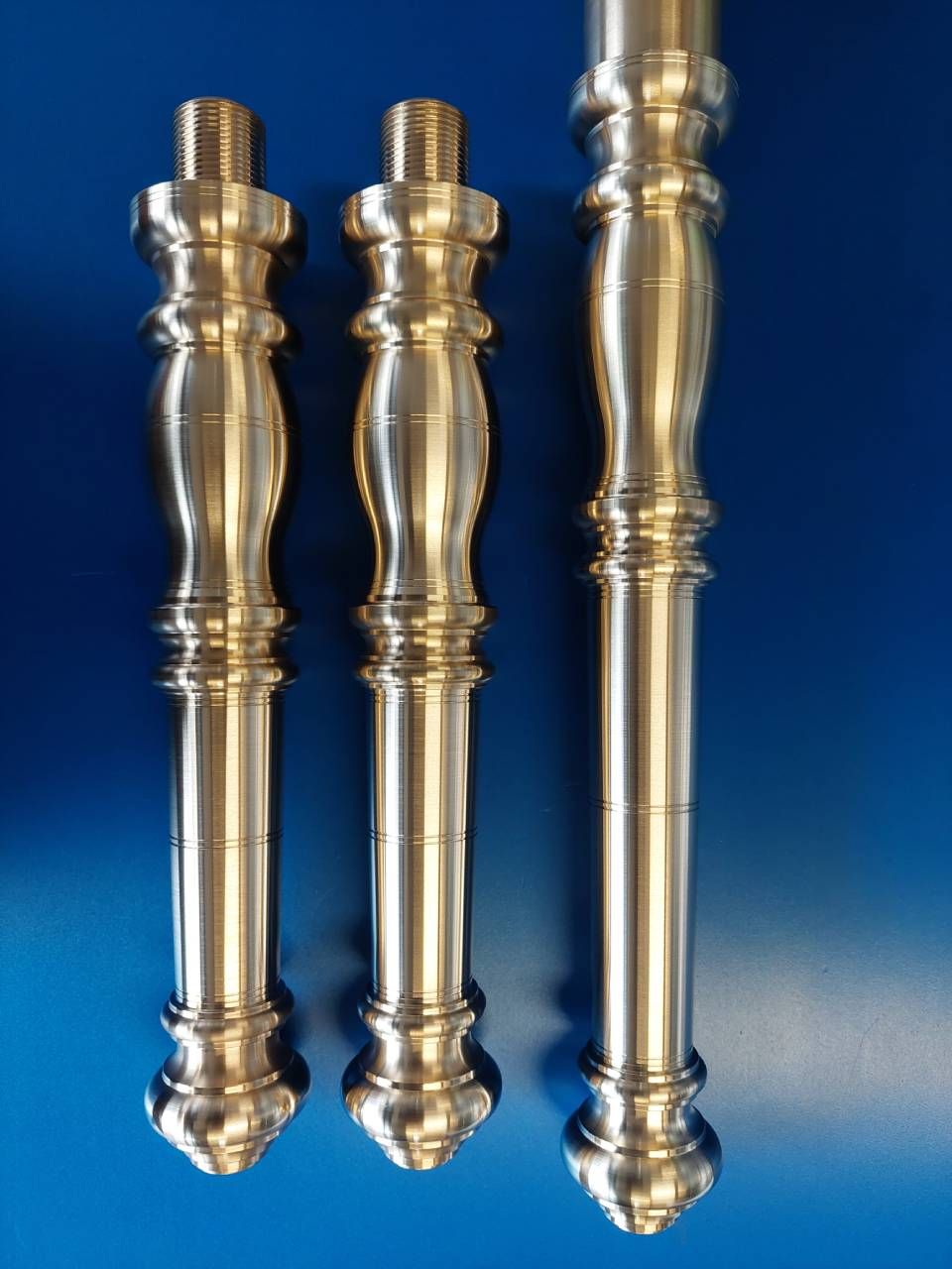 Drei silberne Zierpfosten aus Metall mit kunstvollen, gedrechselten Verzierungen vor blauem Hintergrund.