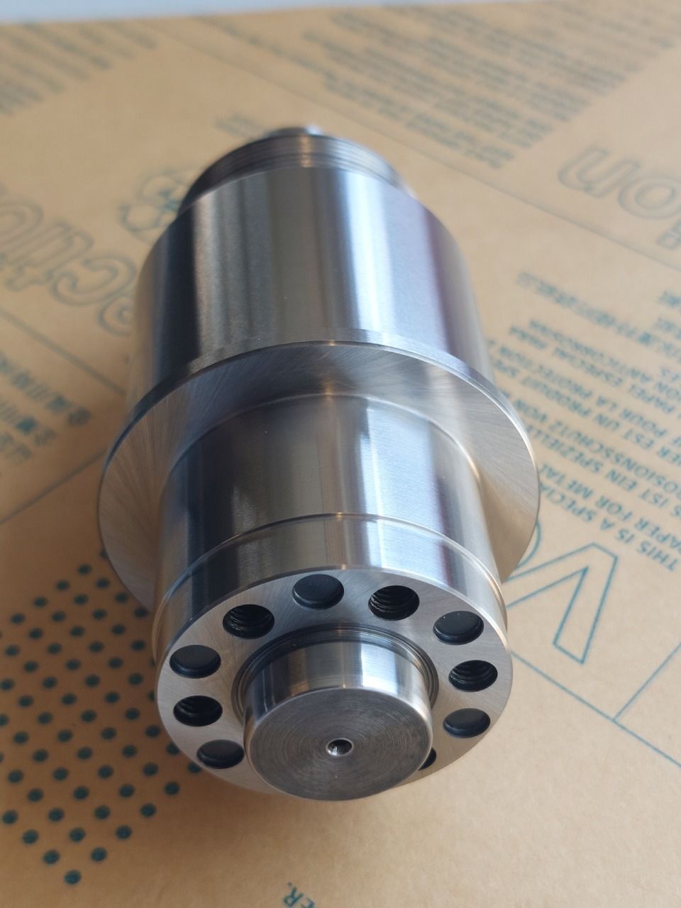 Metallenes zylindrisches Industrieteil mit mehreren Löchern um ein zentrales kreisförmiges Element.