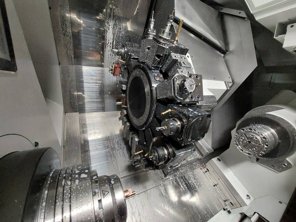 Eine CNC-Maschine ist in Betrieb, an der ein rotierendes Werkstück bearbeitet wird. Kühlmittel ist vorhanden.