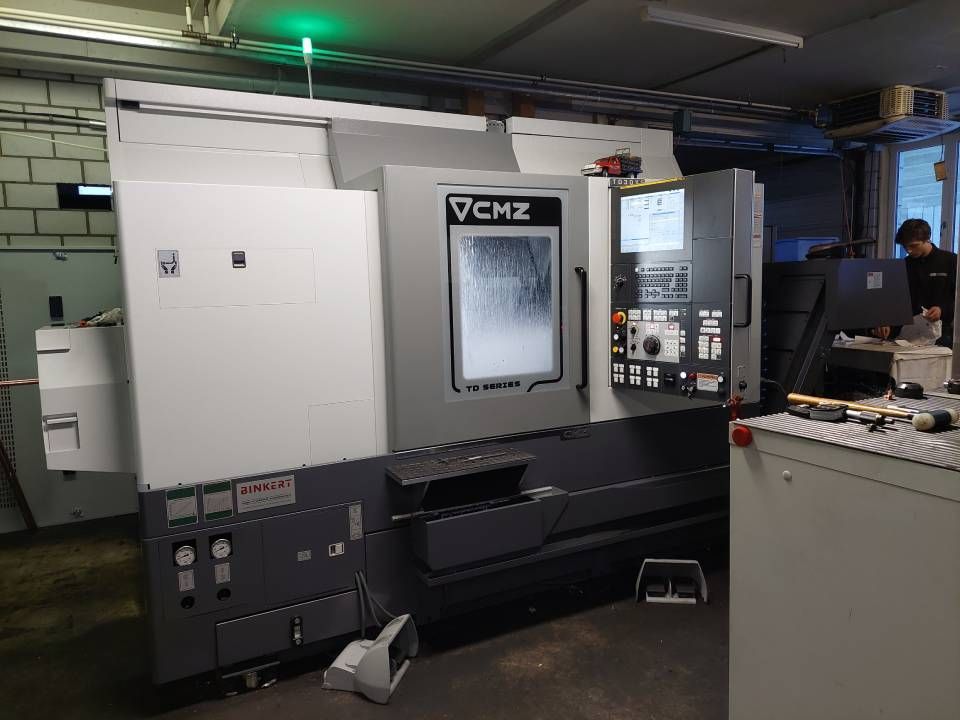 Eine CNC-Fräsmaschine in Grau und Schwarz steht in einer Werkstatt. Im Hintergrund ist eine Person zu sehen.