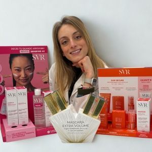 Giovane donna sorridente con capelli lunghi e biondi, circondata da prodotti per la cura della pelle SVR.