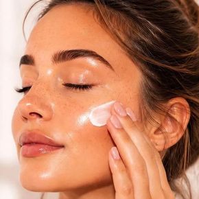 Mujer aplicándose crema blanca en la mejilla favoreciendo el cuidado facial.