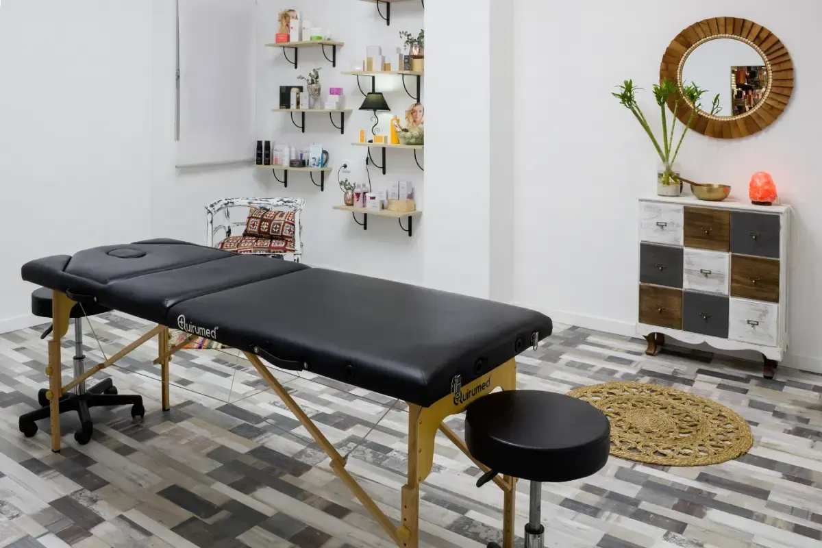 Una camilla de masaje negra en un estudio luminoso y moderno con paredes blancas, estantes con productos