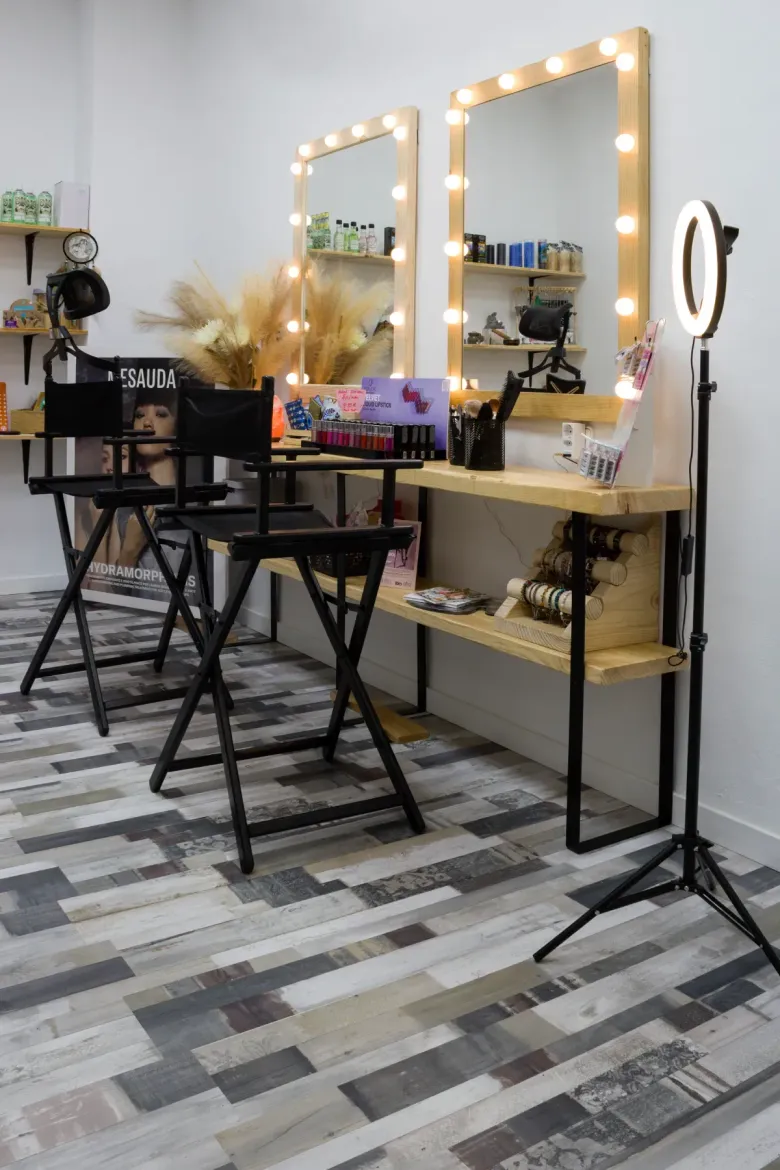 Un estudio de maquillaje profesional con dos sillas altas negras, espejos de tocador con bombillas