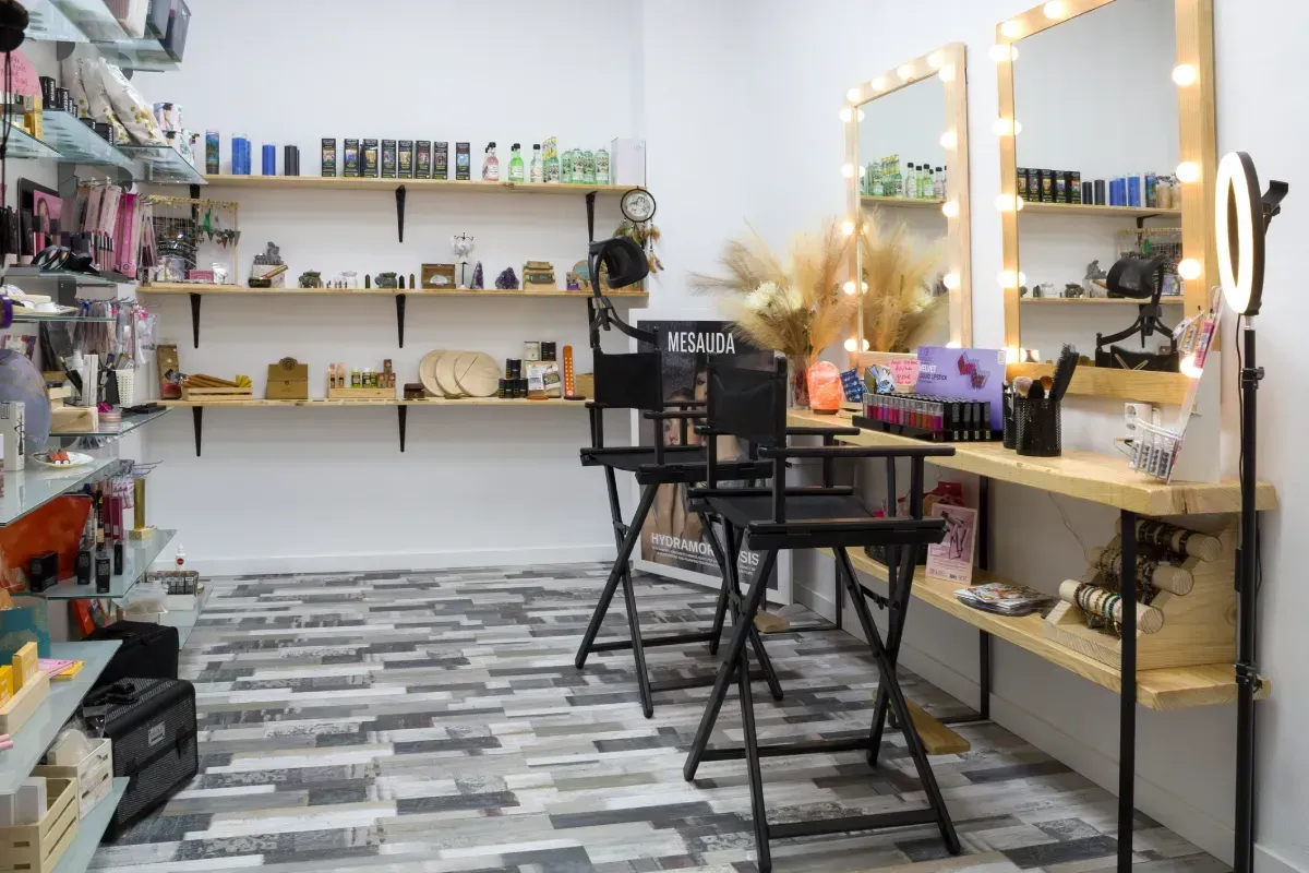 Un estudio de belleza bien iluminado con estantes llenos de productos, dos sillones de maquillaje altos