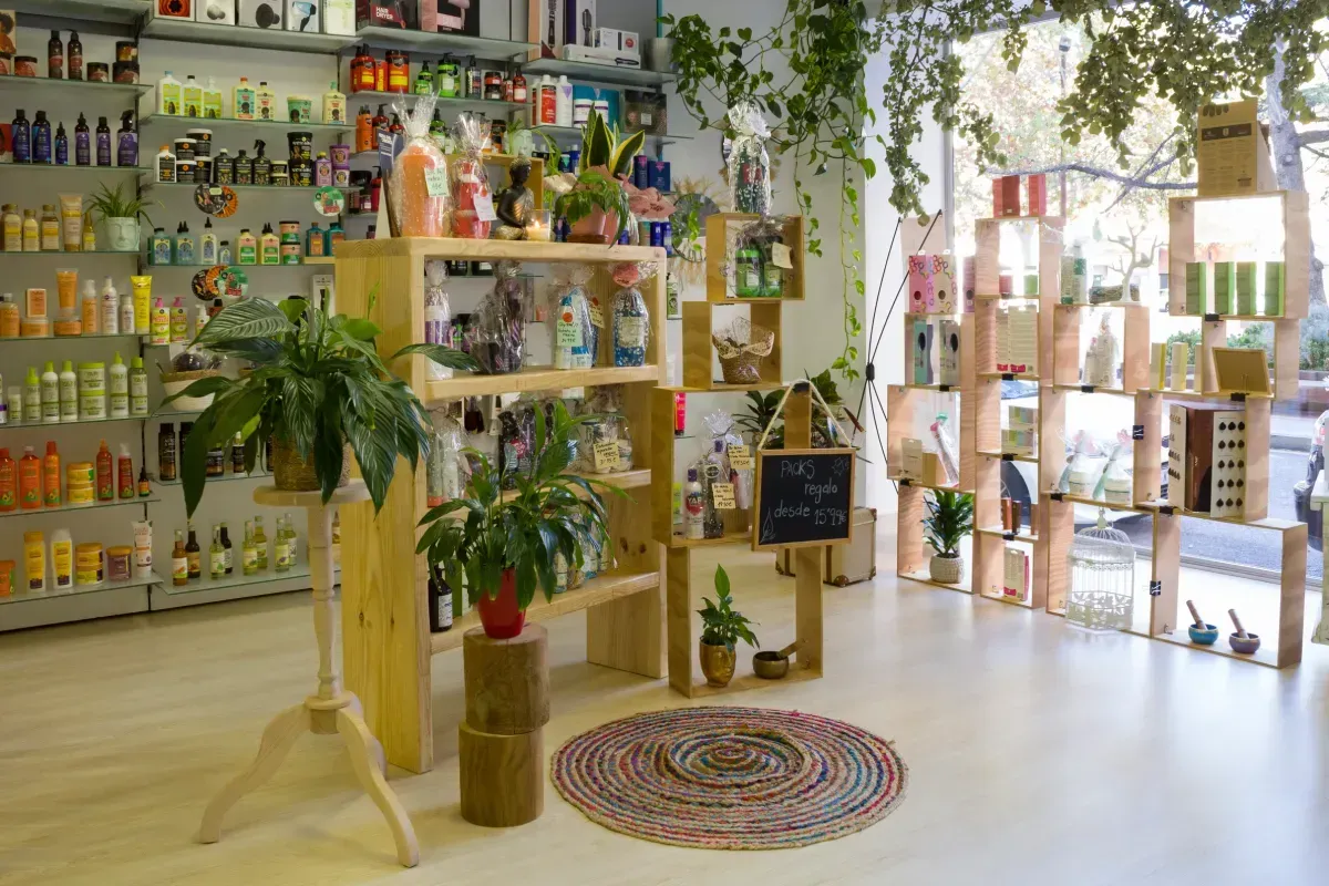 El interior de una tienda bien iluminada cuenta con estanterías de madera repletas de diversos productos, plantas en macetas