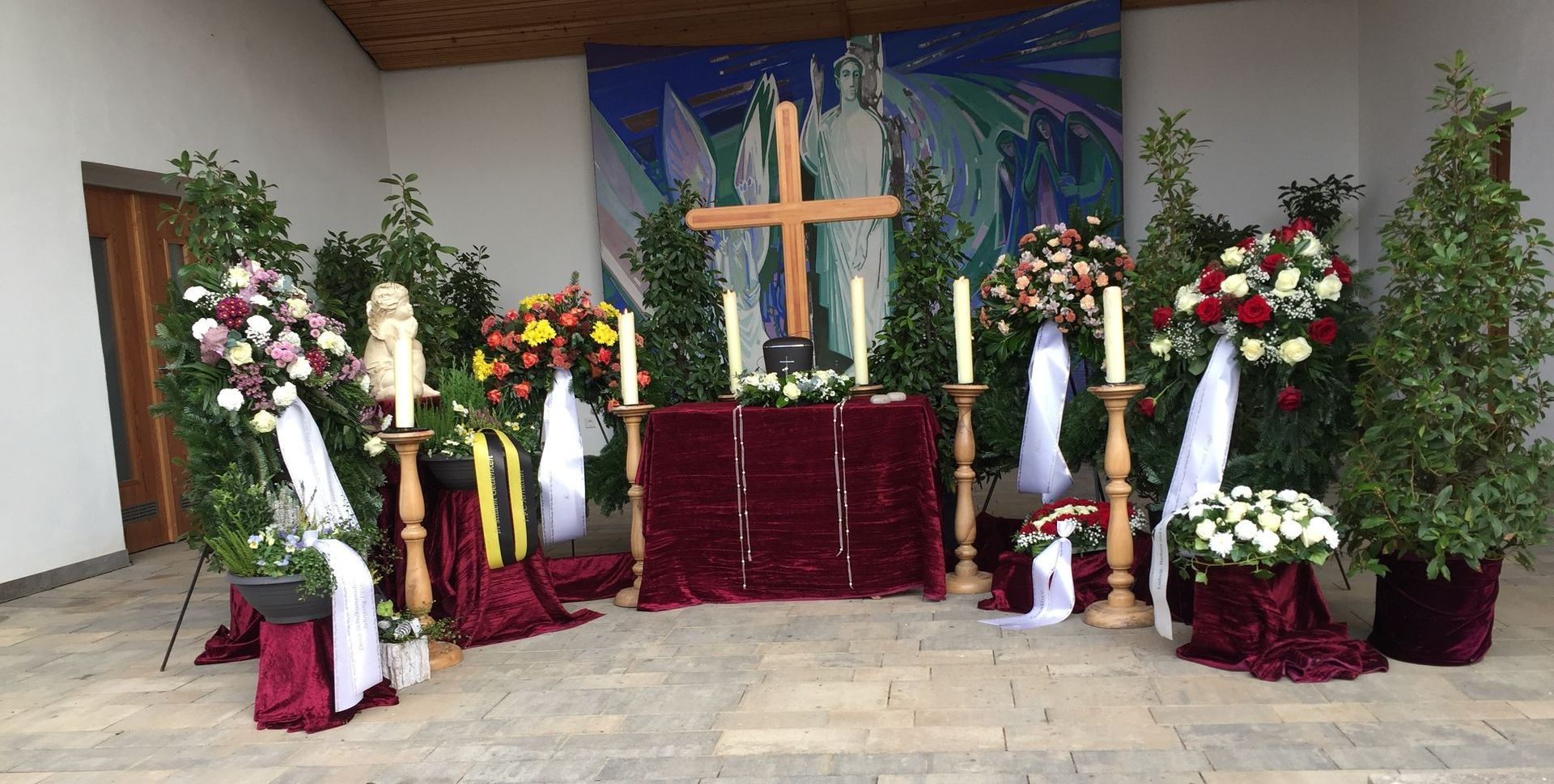 Traueraltar mit Kreuz, Blumen, Kerzen und burgunderfarbenem Tisch.