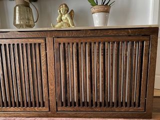 Holzschrank mit Lamellentüren, darauf dekorative Gegenstände: ein Glas, eine Statue und eine Topfpflanze.