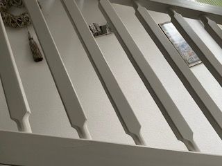 Weiß gestrichenes Treppengeländer. Im Hintergrund ist eine Wand mit Dekorationen zu sehen.