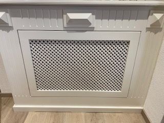 Weiße Heizkörperverkleidung aus Holz mit Gitterrost.