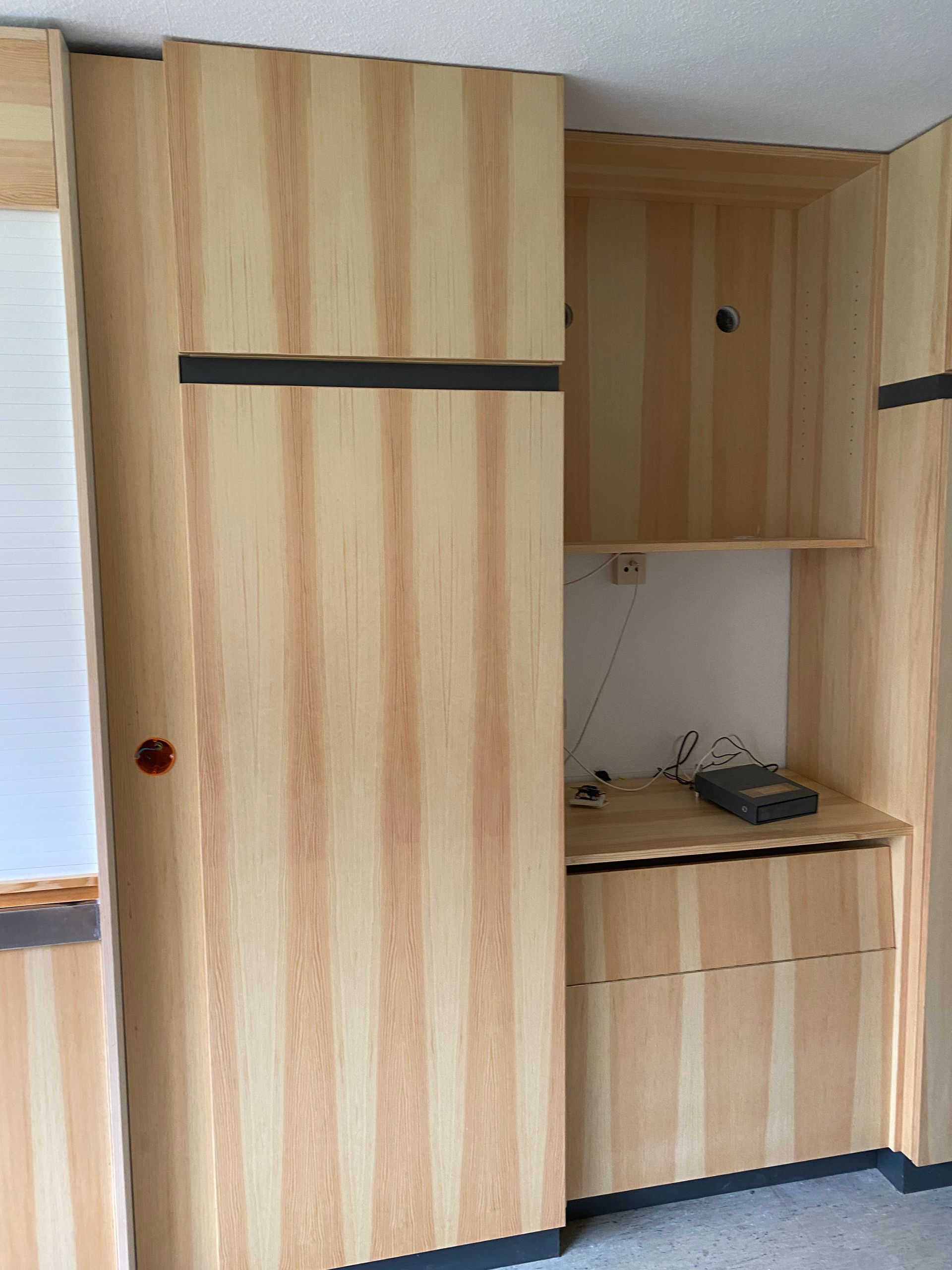 Einbauschrank aus Holz mit offenem Regal, Schublade und Schiebetür. Schwarze horizontale Akzente.