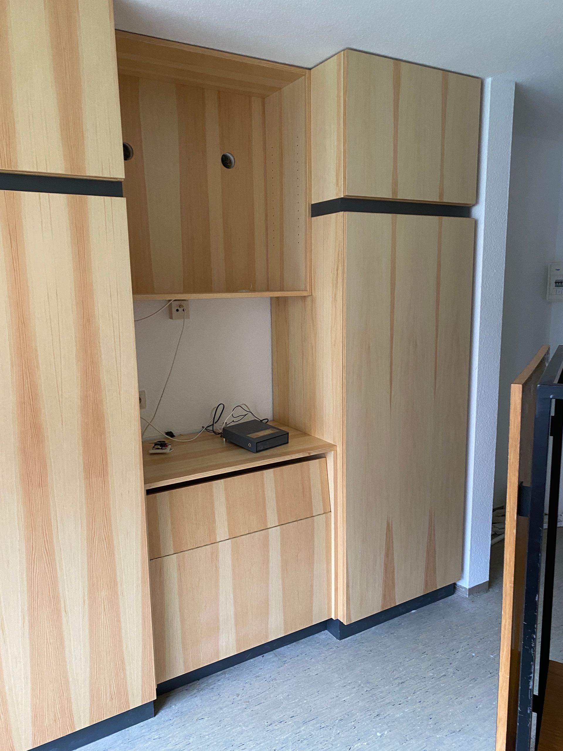 Aufbewahrungseinheit aus Holz mit Schränken, Regalen und Schubladen in einem Wohnbereich.