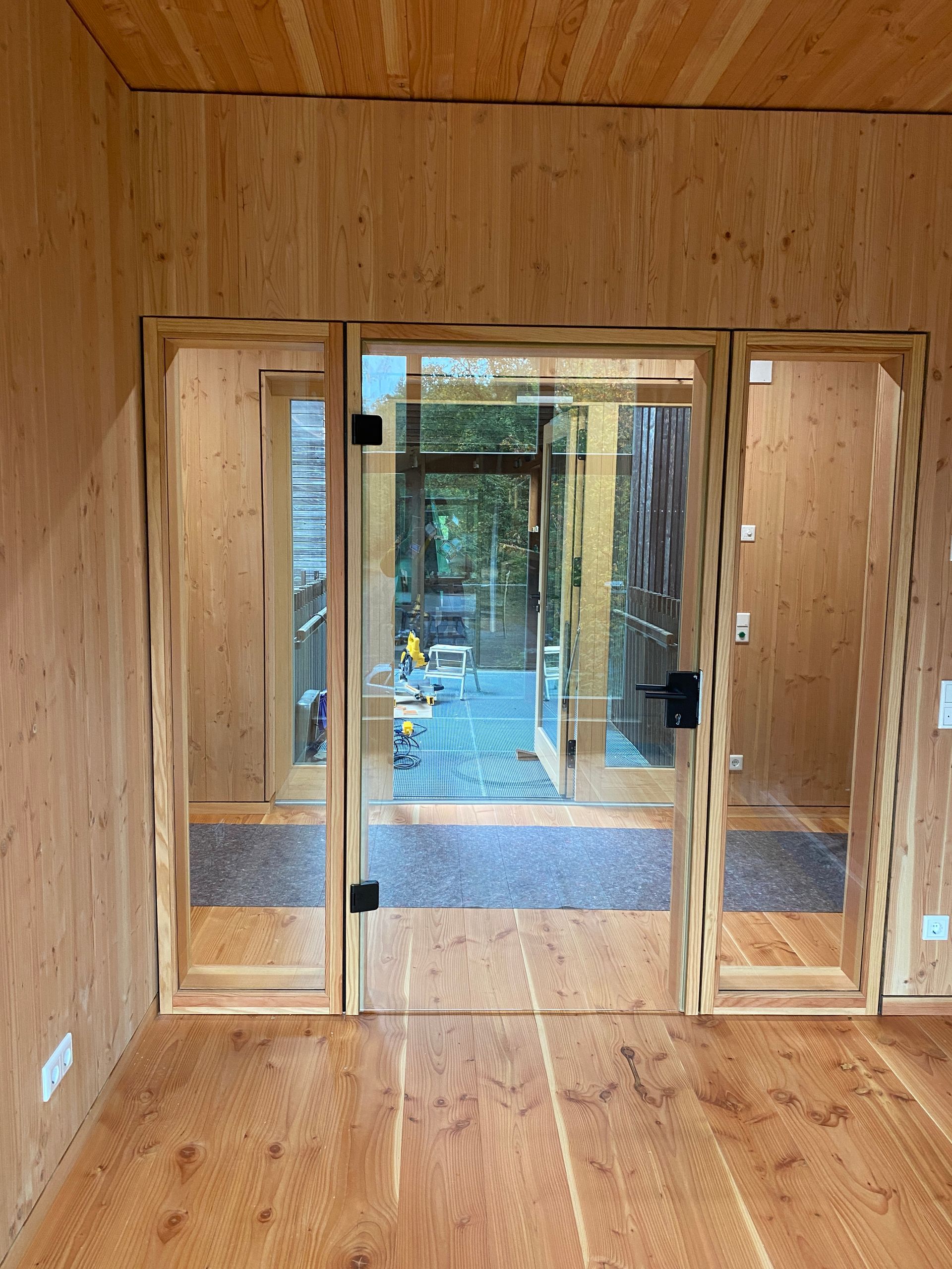 Innenansicht: Glastür mit Holzrahmen; Blick nach außen, holzgetäfelte Wände.