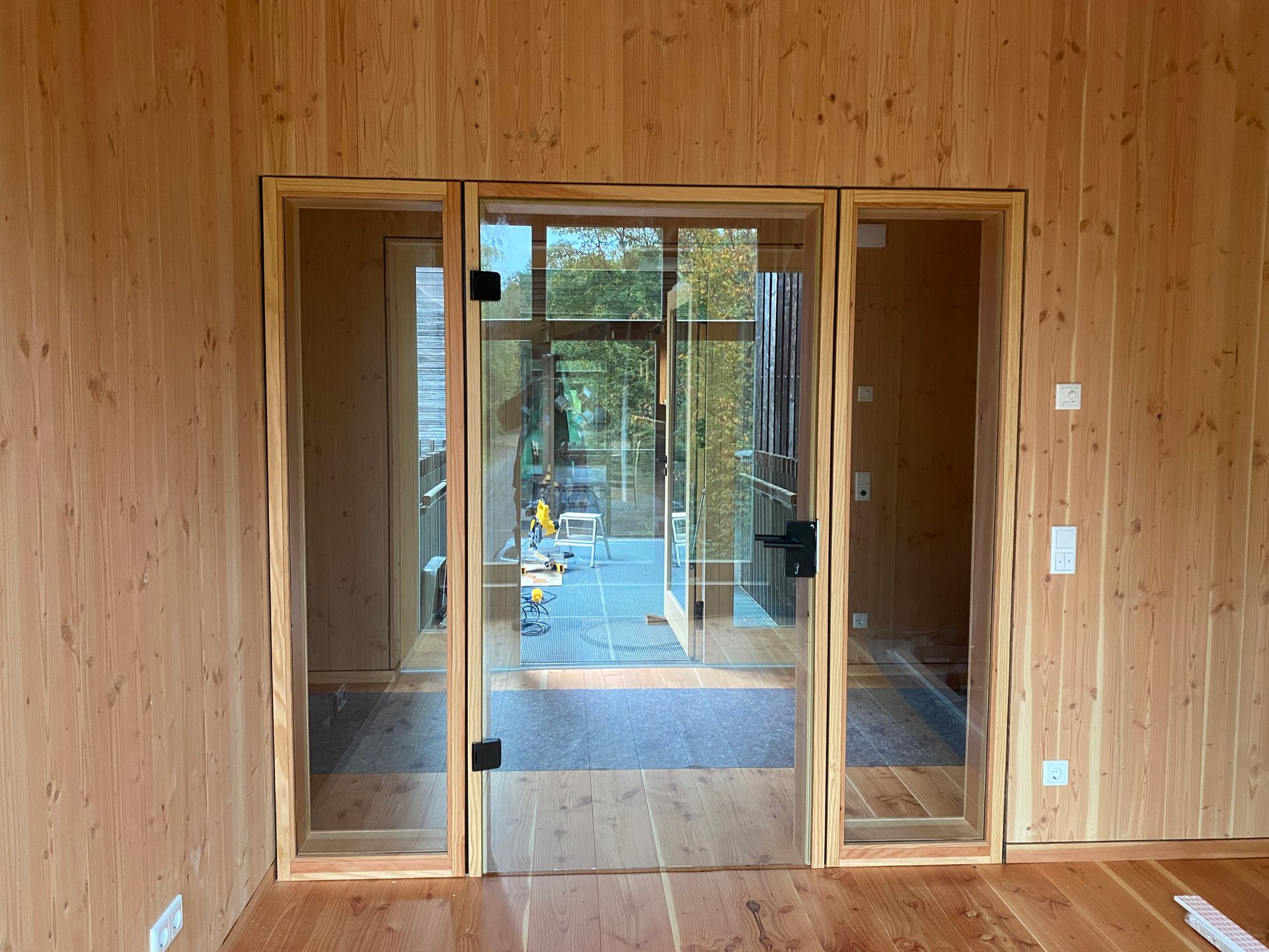 Glastüren mit Holzrahmen und Seitenlichter in einem holzgetäfelten Raum, der zu einer Außenterrasse führt.