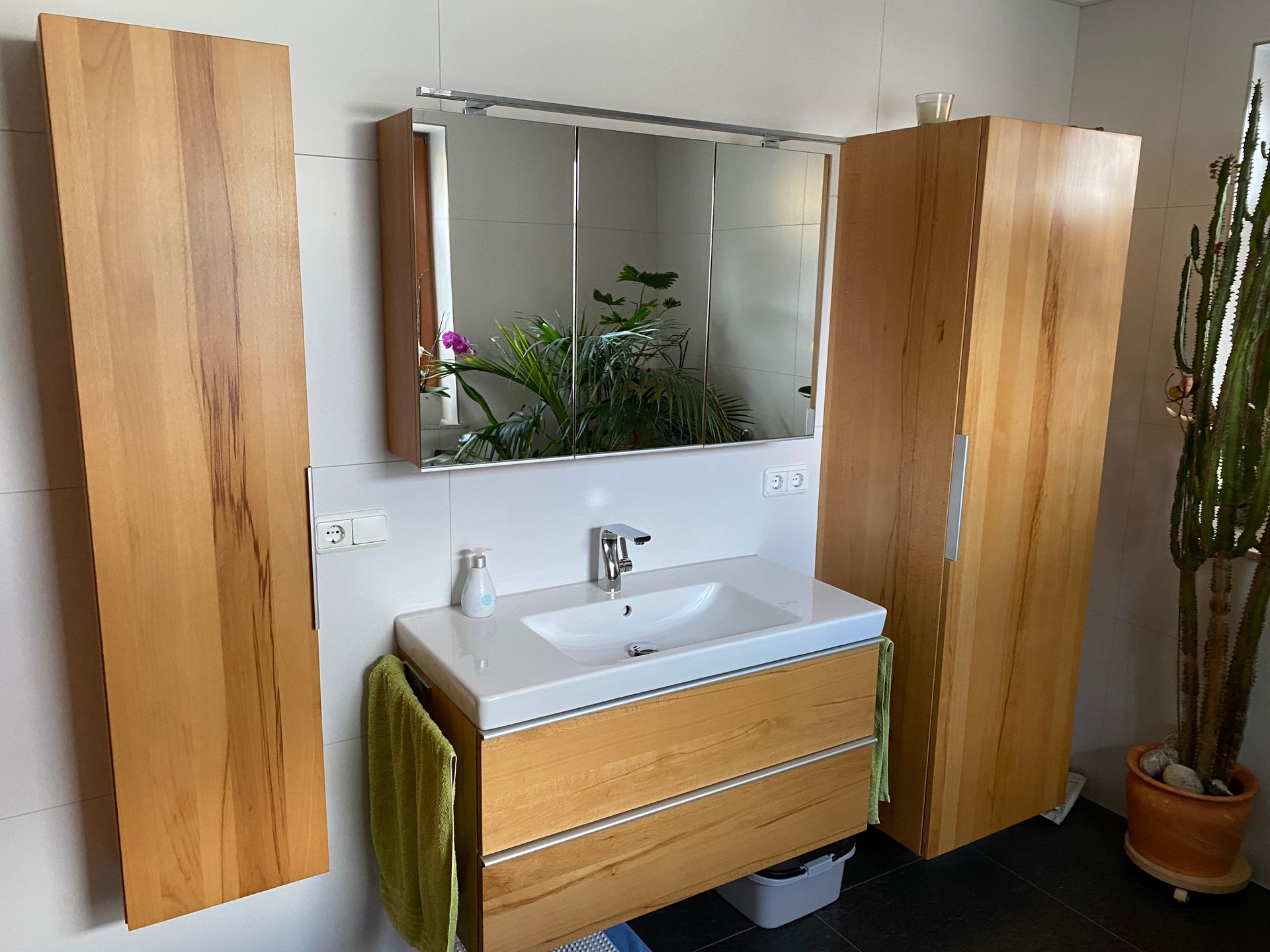 Badezimmer mit Holzschränken, einem weißen Waschbecken und einem großen Spiegel.