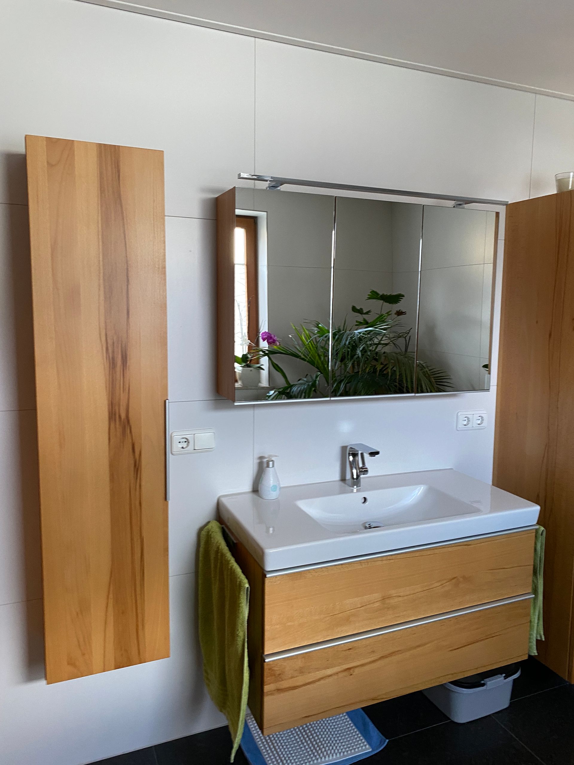 Modernes Badezimmer mit Holzwaschtisch, Spiegelschrank und hohem Stauraum. In der Mitte befindet sich ein Waschbecken.