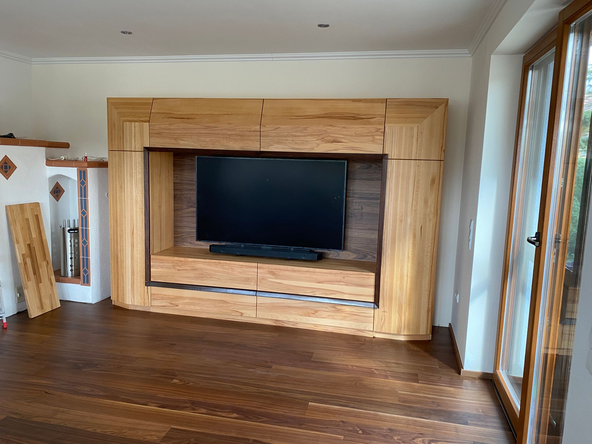 Fernsehschrank aus Holz mit integrierter Soundbar und Schubladen vor einer Holzwand.
