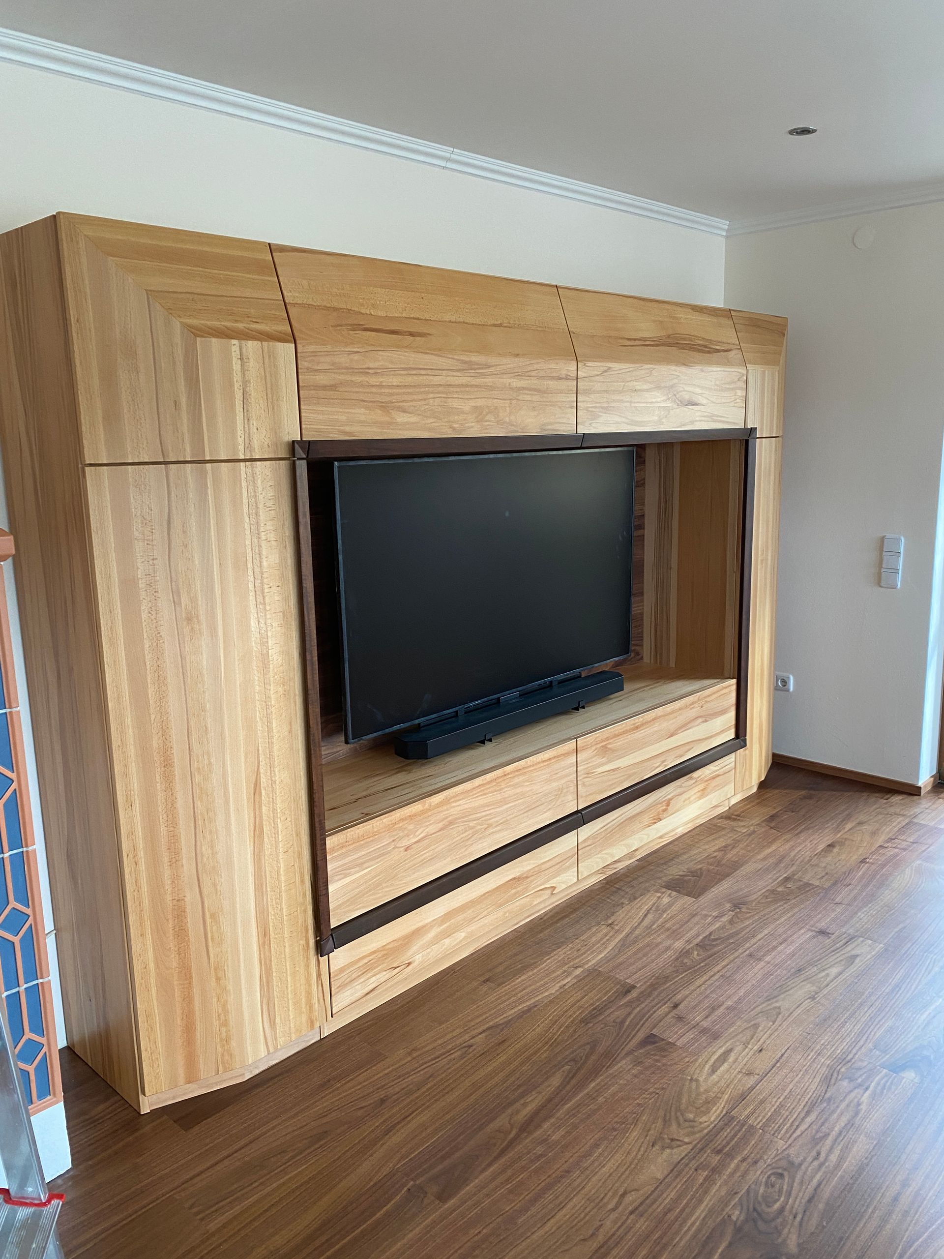 Entertainment-Center aus Holz mit Fernseher in einer Nische an einer hellen Wand montiert; Holzboden.