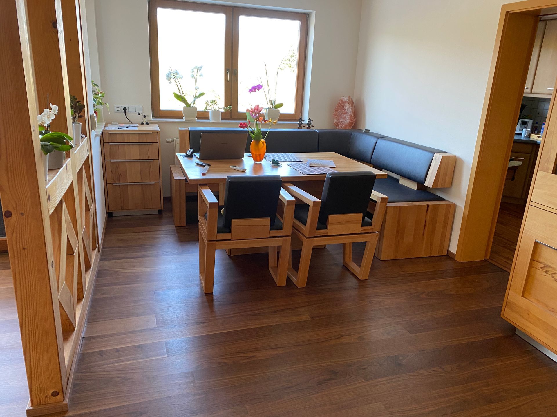 Essbereich mit Holztisch, schwarzer gepolsterter Bank, Stühlen und Holzboden.