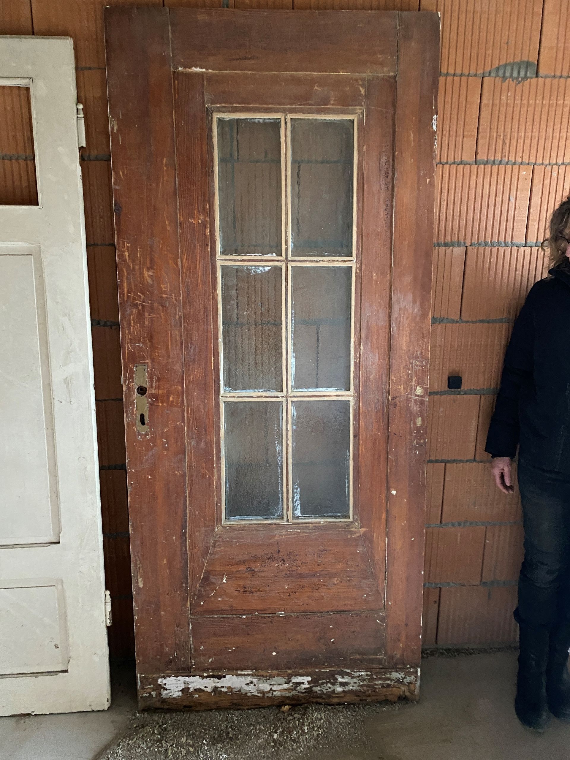 Alte Holztür mit Glasscheiben neben einer Person. Die Tür ist braun und die Farbe blättert ab.