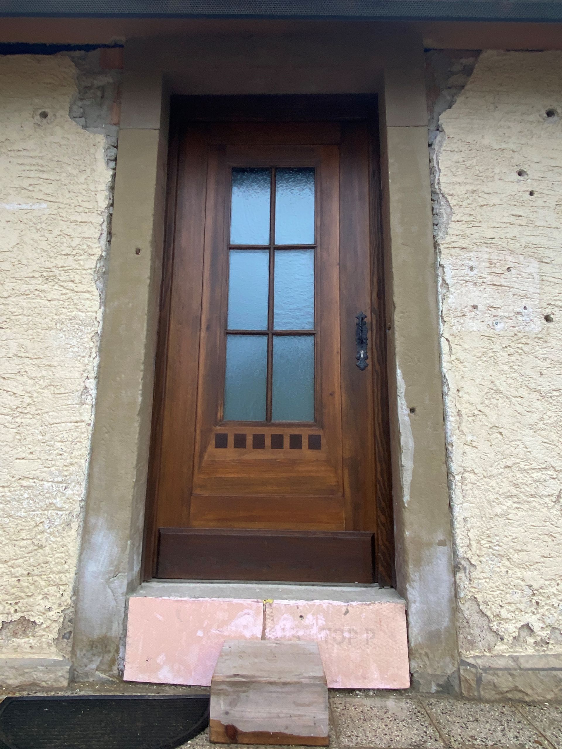 Holztür mit Glasscheiben und Stufe. Beigefarbene Gebäudefassade.