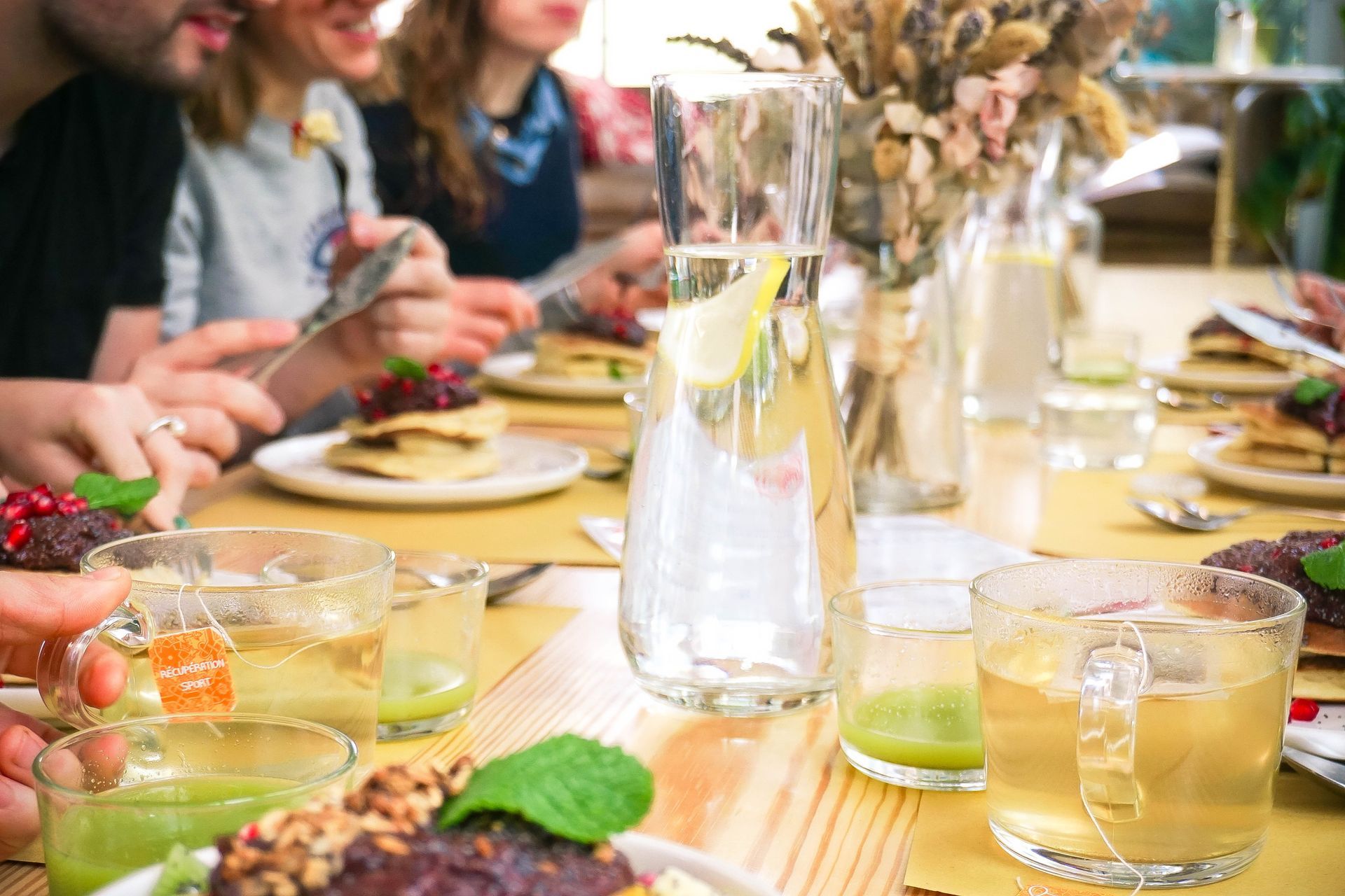 Des personnes dînent à une table avec des boissons, des assiettes et des fleurs dans un restaurant.