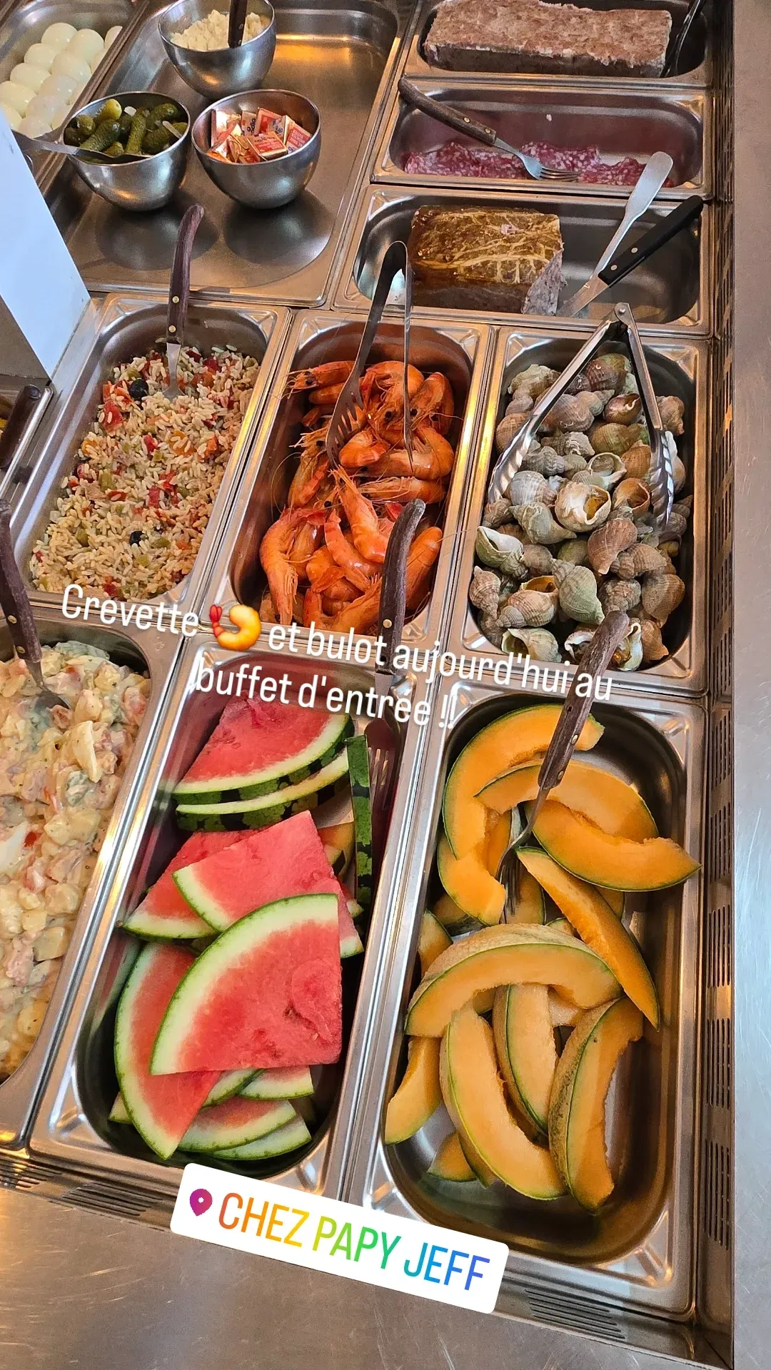 Buffet coloré de plats préparés, comprenant des tranches de pastèque, des raisins, des légumes, des crevettes et des sauces.