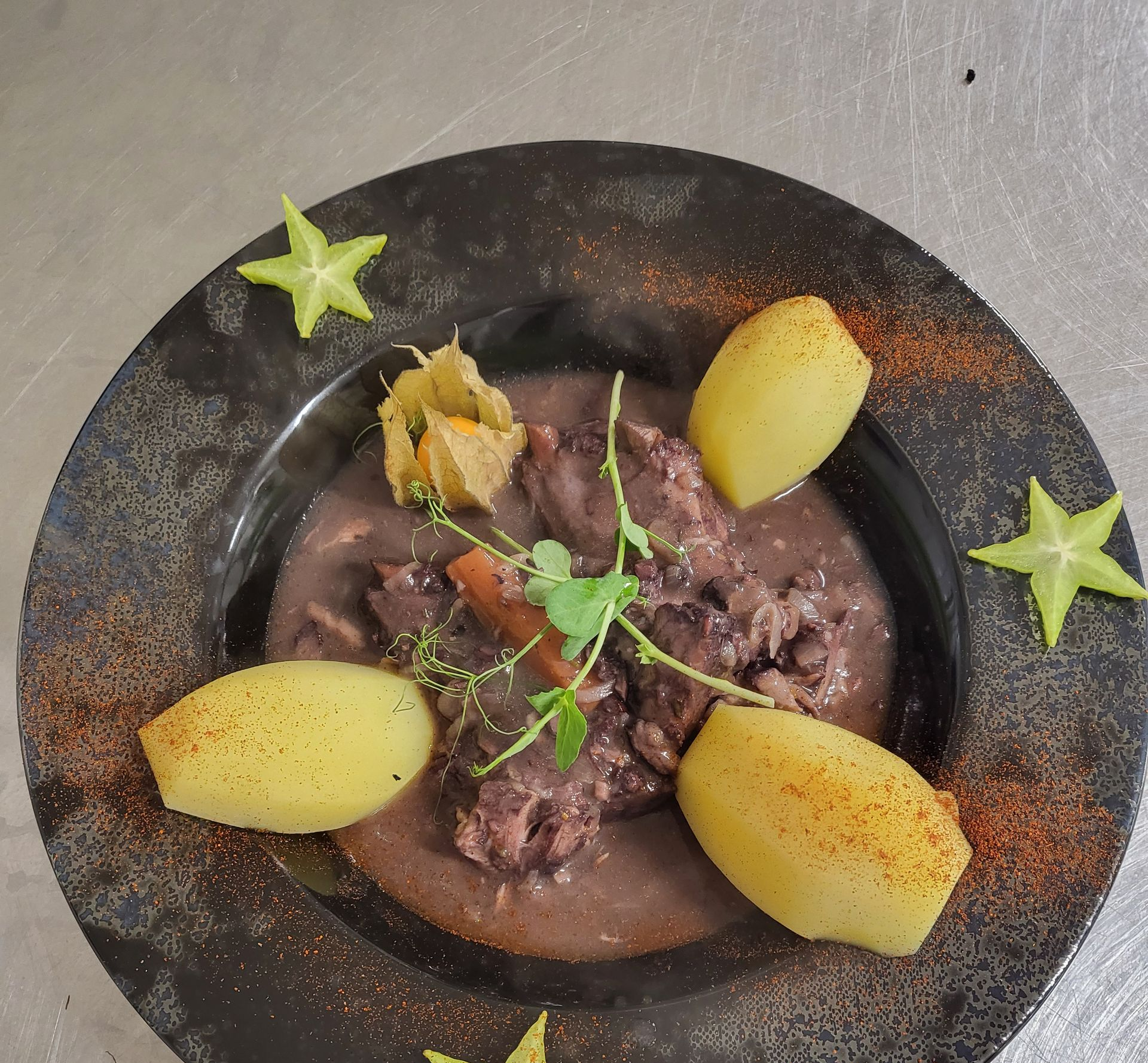 Bol de ragoût garni d'herbes, entouré de quartiers de poire et d'une garniture en forme d'étoile, présenté dans une assiette.