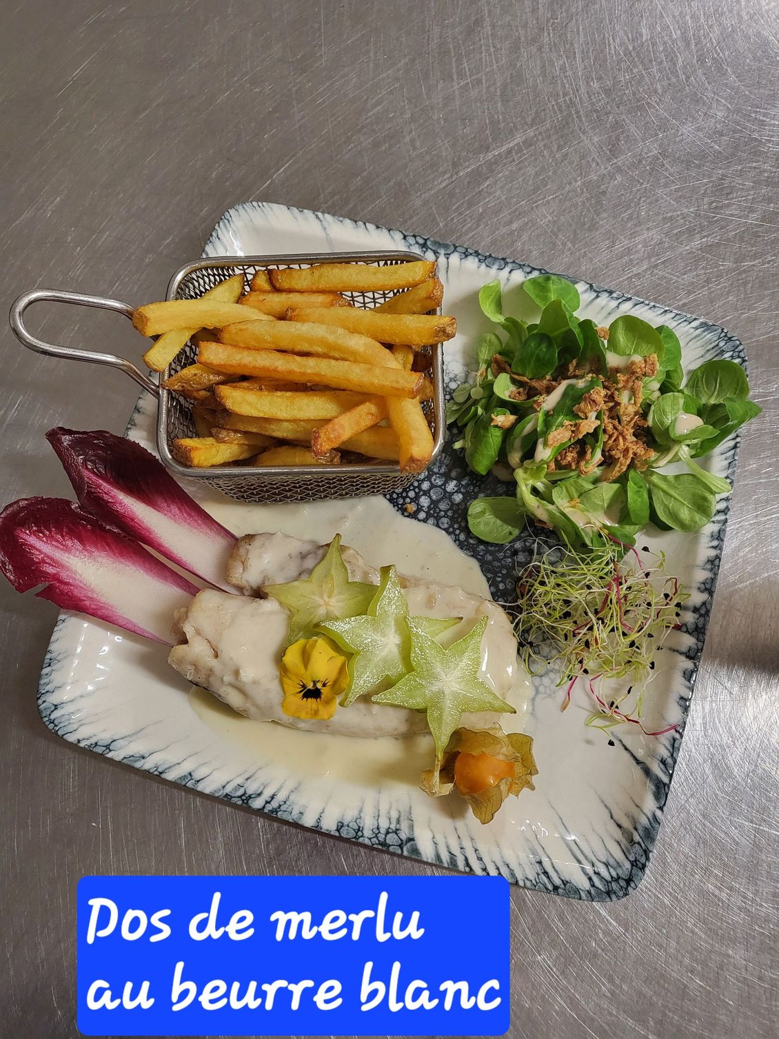 Assiette de dos de merlu au beurre avec frites, salade et garniture colorée.