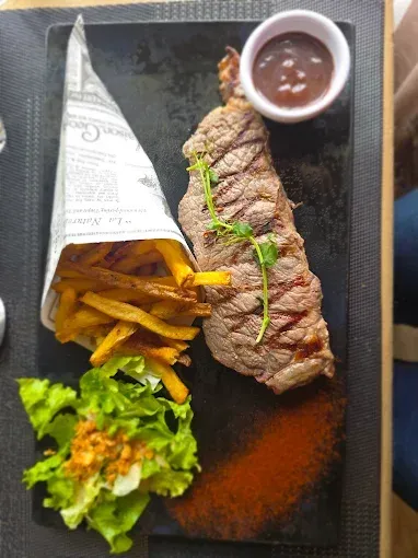 Repas de steak avec frites, salade et sauce, servi dans une assiette.