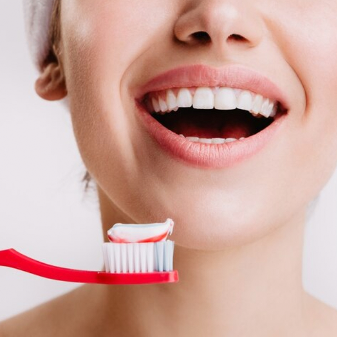 Una persona che sorride con un sorriso smagliante, tenendo in mano uno spazzolino rosso con dentifricio a strisce rosse e bianche sulle setole.