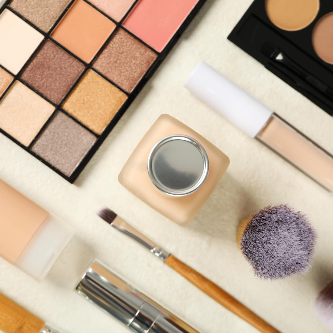 Una vista dall'alto dei cosmetici, tra cui una palette di ombretti, un fondotinta liquido, un correttore e dei pennelli per il trucco.