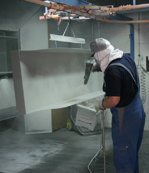 Ein Mann in Overalls und Maske sprüht Farbe auf ein Stück Metall