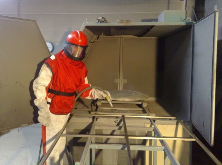 Ein Mann in einem rot-weißen Anzug sandstrahlt ein Stück Metall