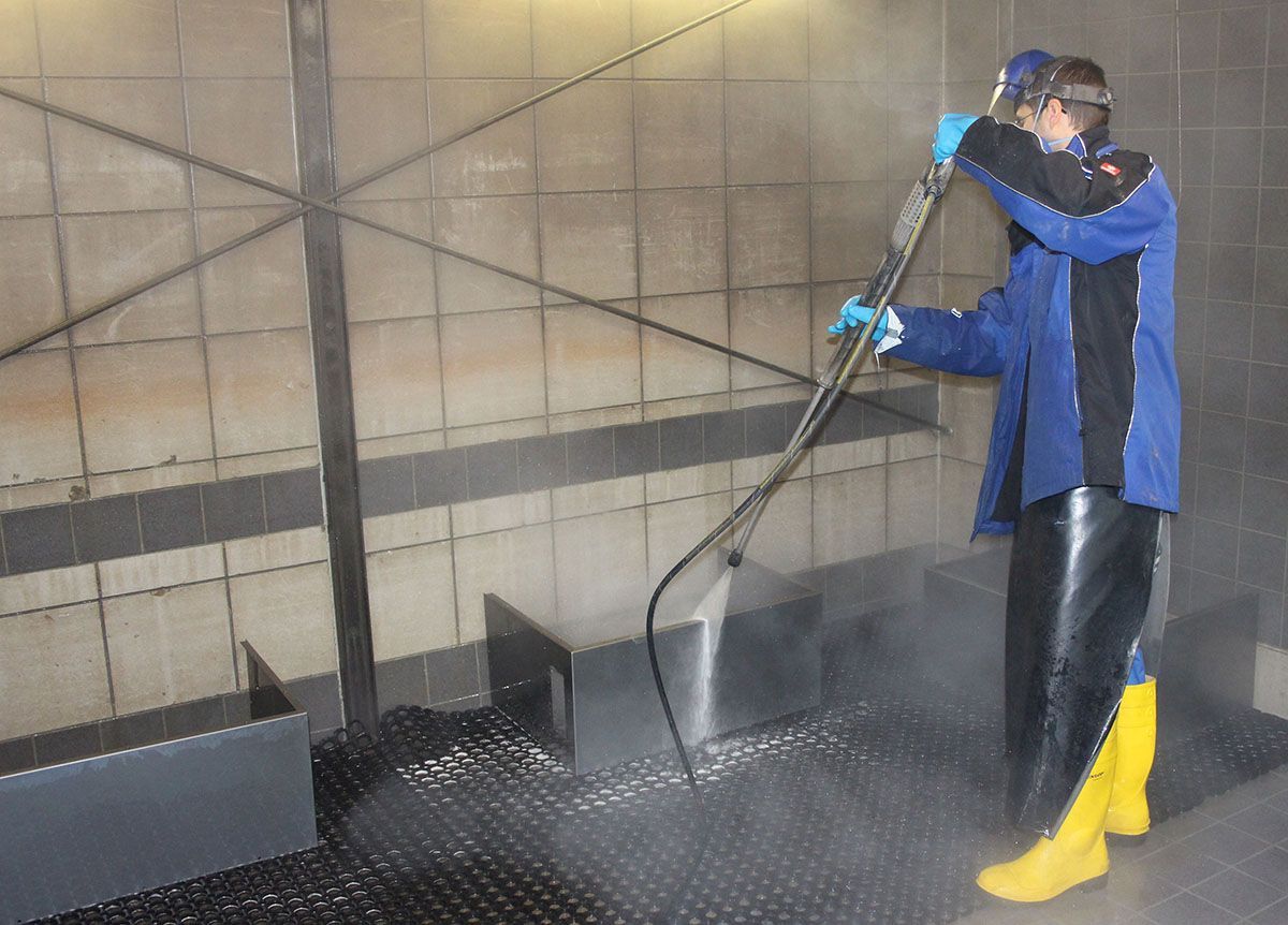 Ein Mann in einer blauen Jacke und gelben Stiefeln benutzt einen Hochdruckreiniger.