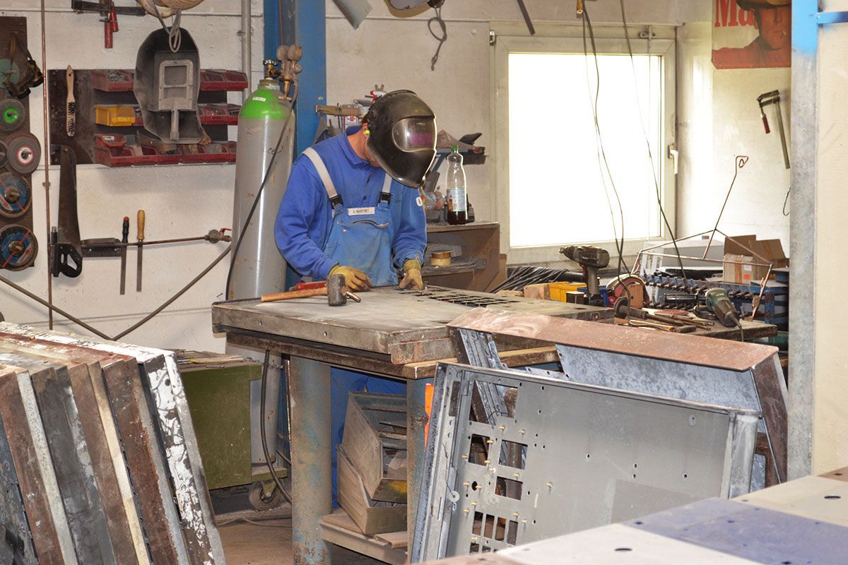 Ein Mann mit Schweißhelm arbeitet in einer Werkstatt an einem Metallstück.