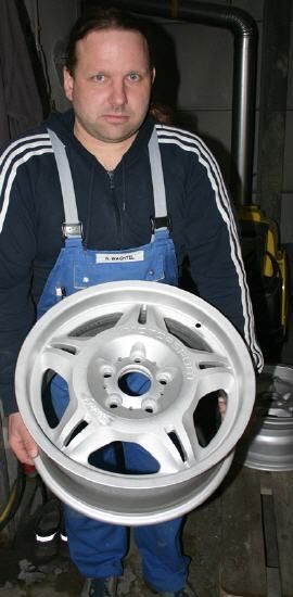 Ein Mann im blauen Overall hält einen silbernen Rand