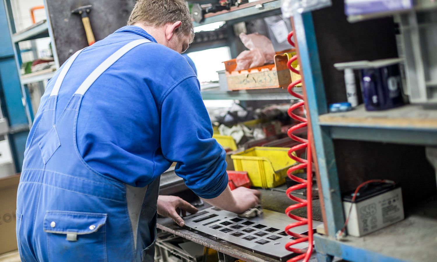 Ein Mann in einem blauen Overall arbeitet in einer Fabrik an einer Maschine.