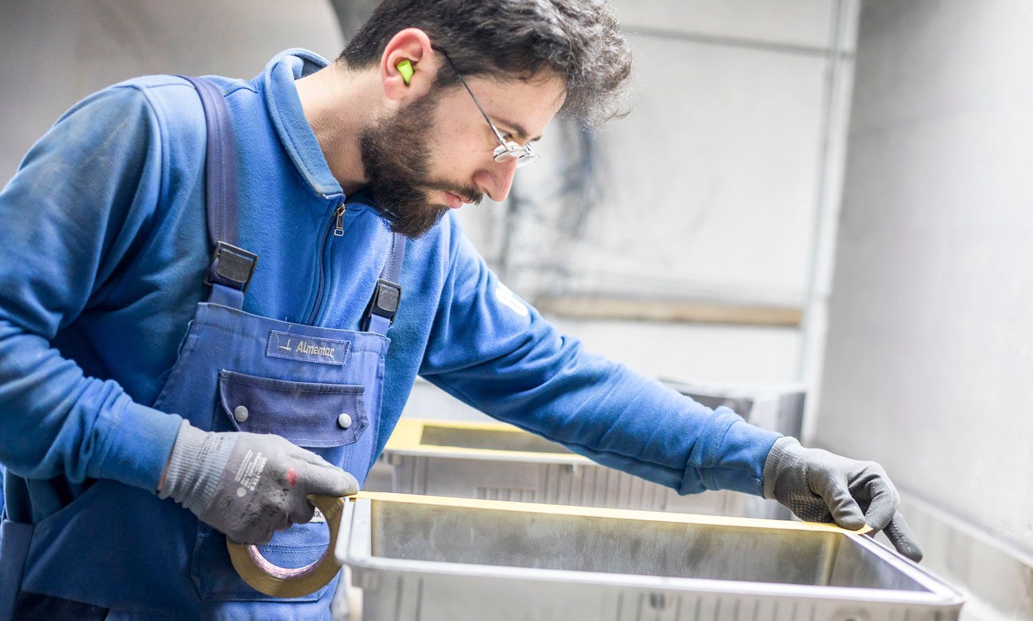Ein Mann in einem blauen Hemd und Overall arbeitet in einer Fabrik.