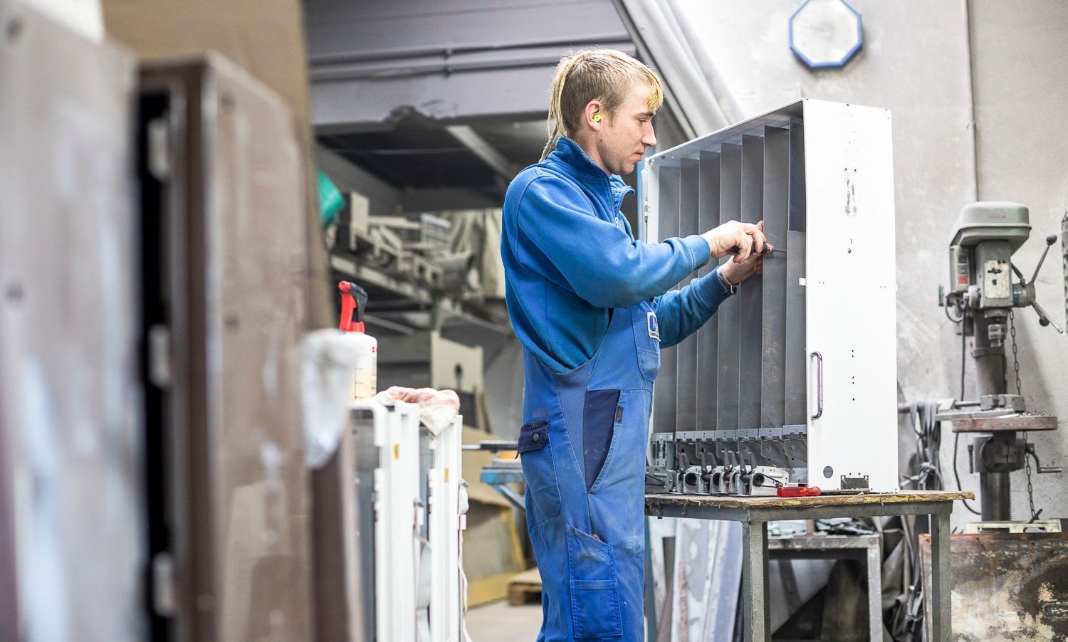 Ein Mann im blauen Overall arbeitet in einer Fabrik an einem Stück Metall.