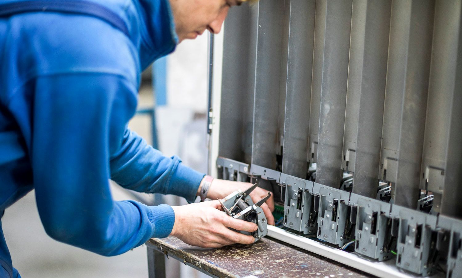 Ein Mann in einem blauen Pullover arbeitet in einer Fabrik an einer Maschine.
