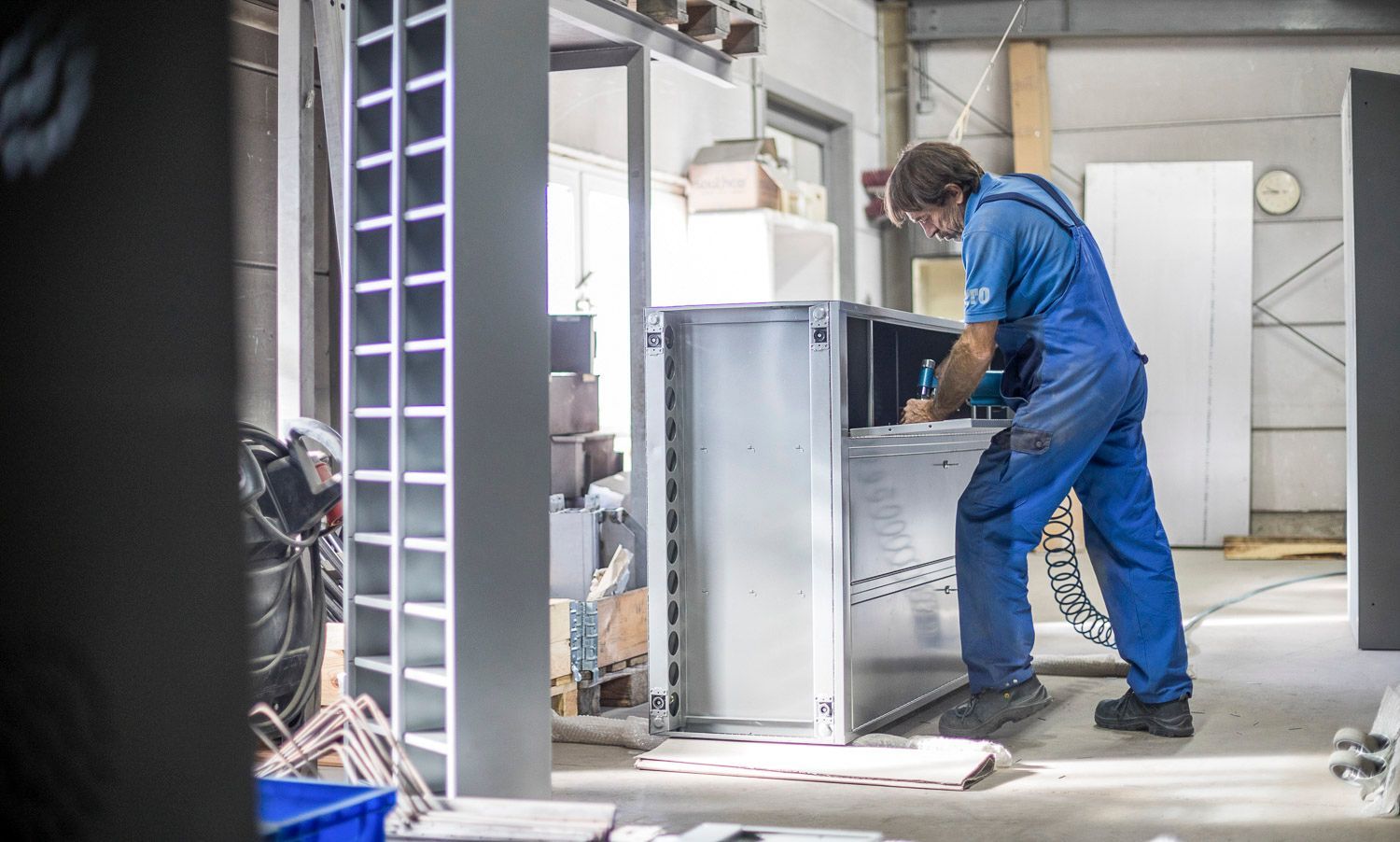 Ein Mann im blauen Overall arbeitet in einer Fabrik an einem Metallschrank.