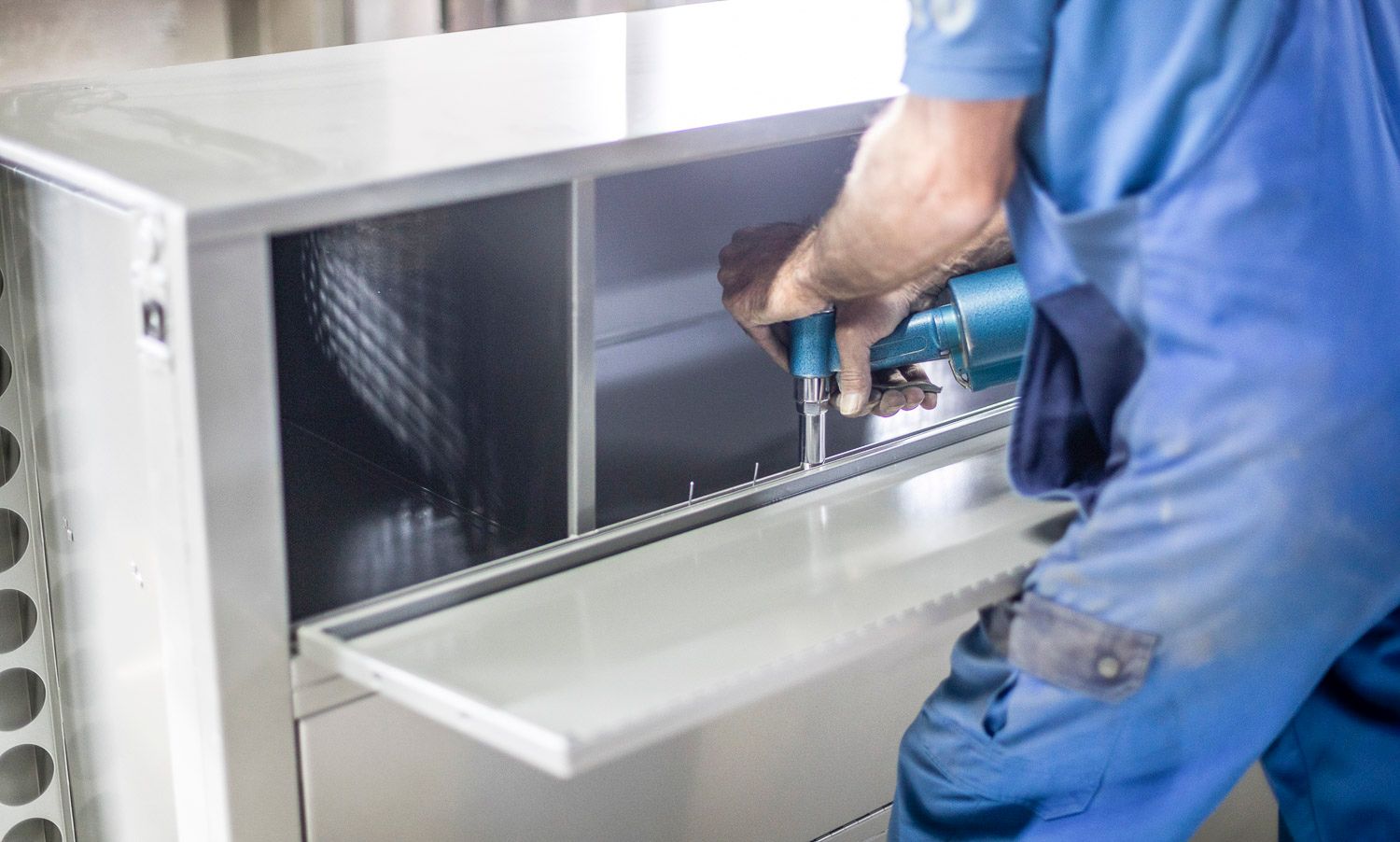 Ein Mann im blauen Overall arbeitet mit einer Bohrmaschine an einer Maschine.