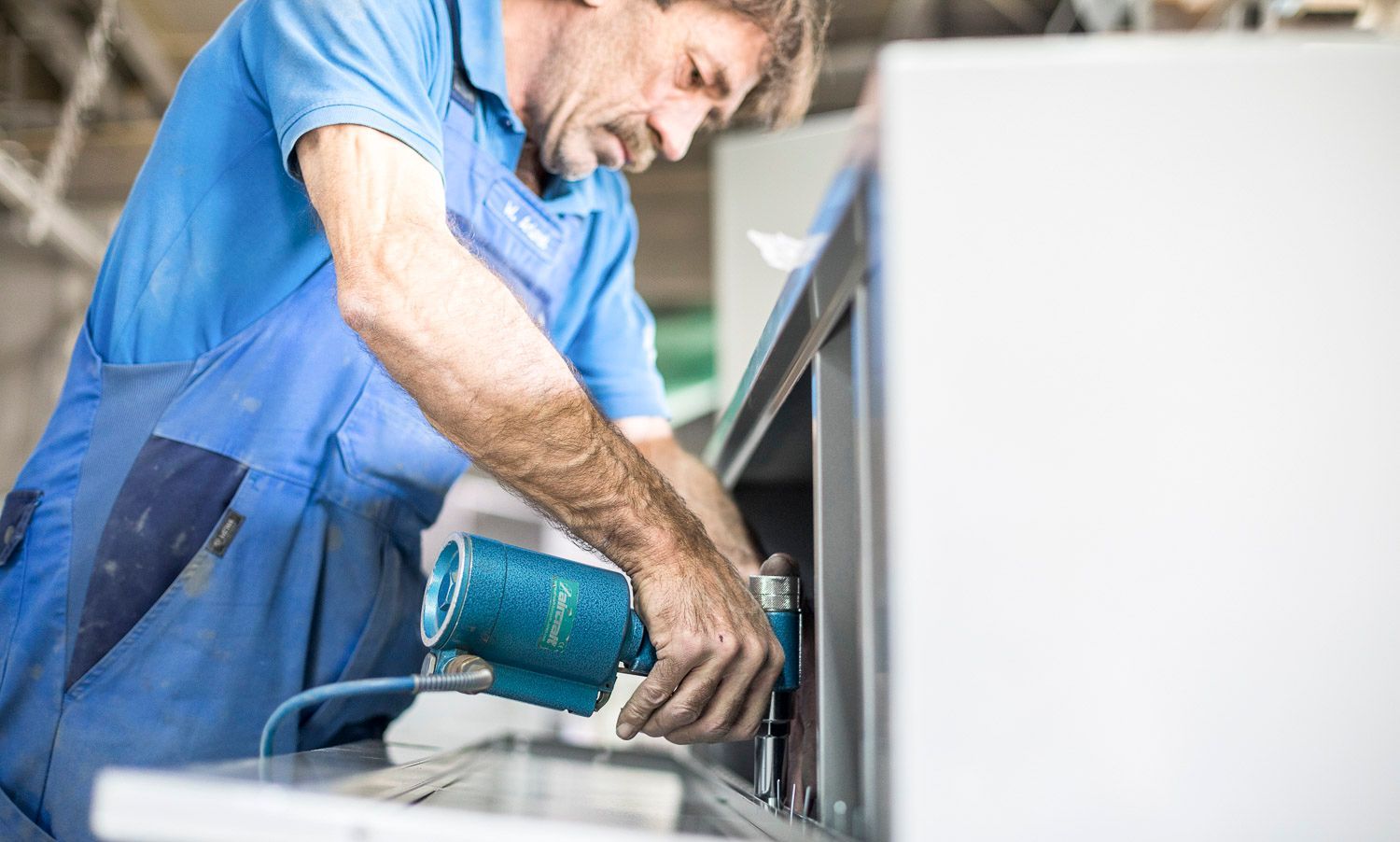 Ein Mann in einem blauen Hemd arbeitet in einer Fabrik an einer Maschine.