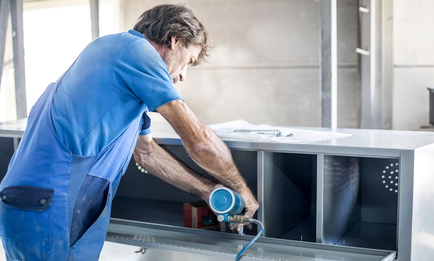 Ein Mann in einem blauen Hemd arbeitet an einem Stück Metall.