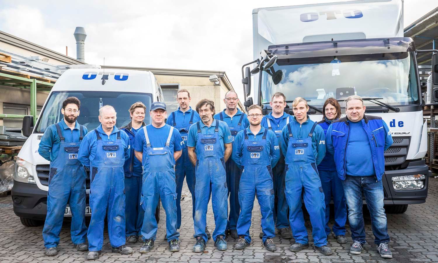 Eine Gruppe von Menschen in blauen Overalls posiert vor Lastwagen für ein Foto.