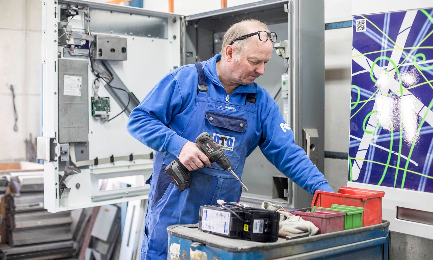Ein Mann in einem blauen Overall arbeitet an einer Maschine mit einer Bohrmaschine.