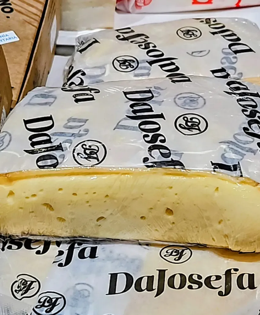 Una porción de pastel amarillo sobre papel de regalo con el logo de la marca, que deja ver un interior cremoso en capas.